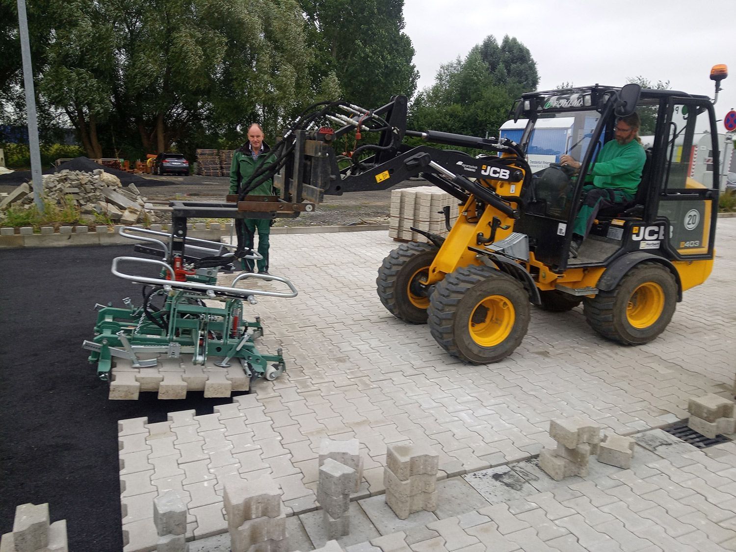 Ein JCB-Gabelstapler wird von einer Person bedient, die mit einem mechanischen Anbaugerät Pflastersteine verlegt