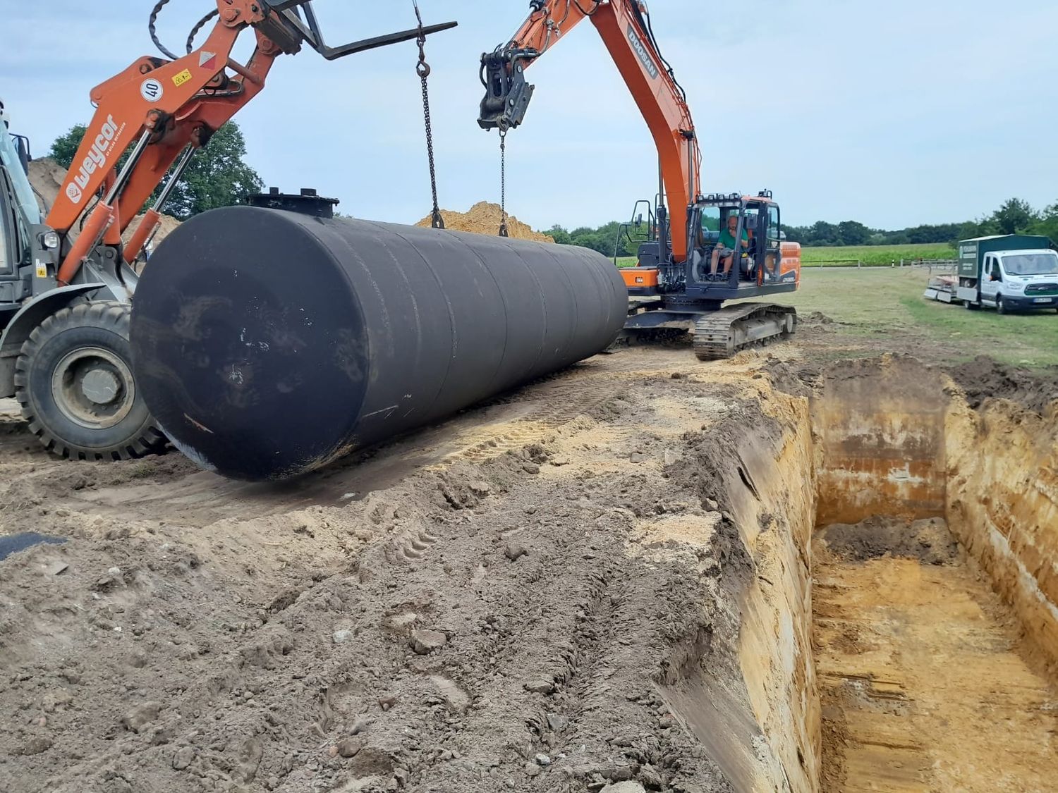 Ein großer schwarzer Tank wird von einem Bagger auf einer Baustelle in eine Baugrube abgesenkt